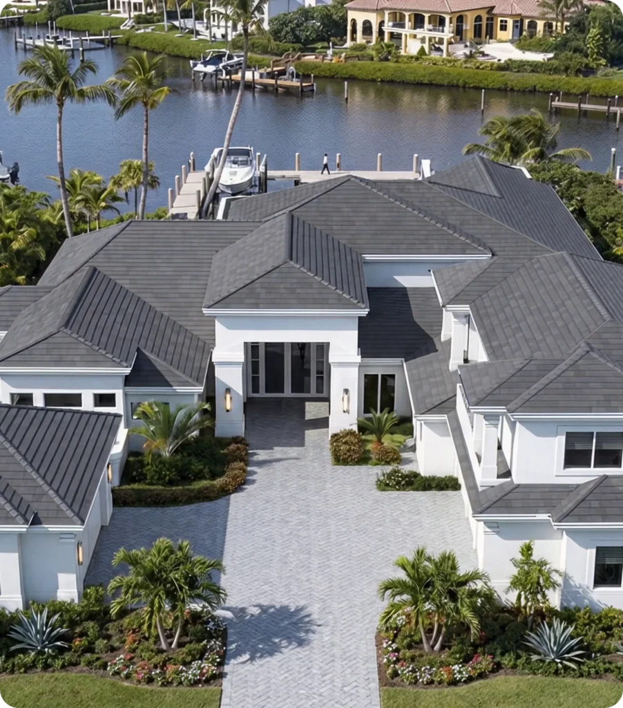 Aerial view of a luxury waterfront home in Miami, FL with a gray tile roof installed by 7Roofing, surrounded by palm trees, landscaping, and a canal.